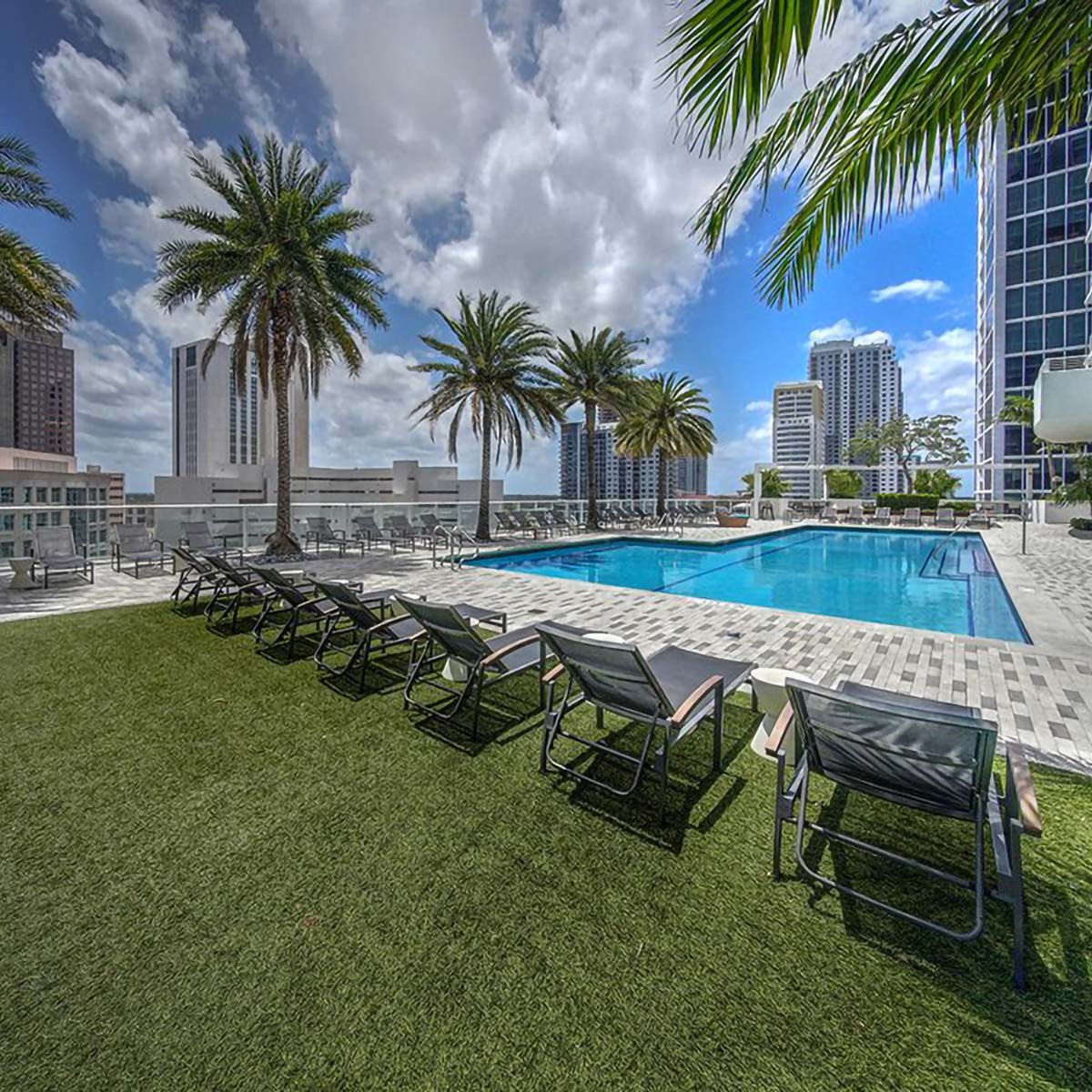 Rooftop pool with green lawn, lounge chairs, and tall palm trees.