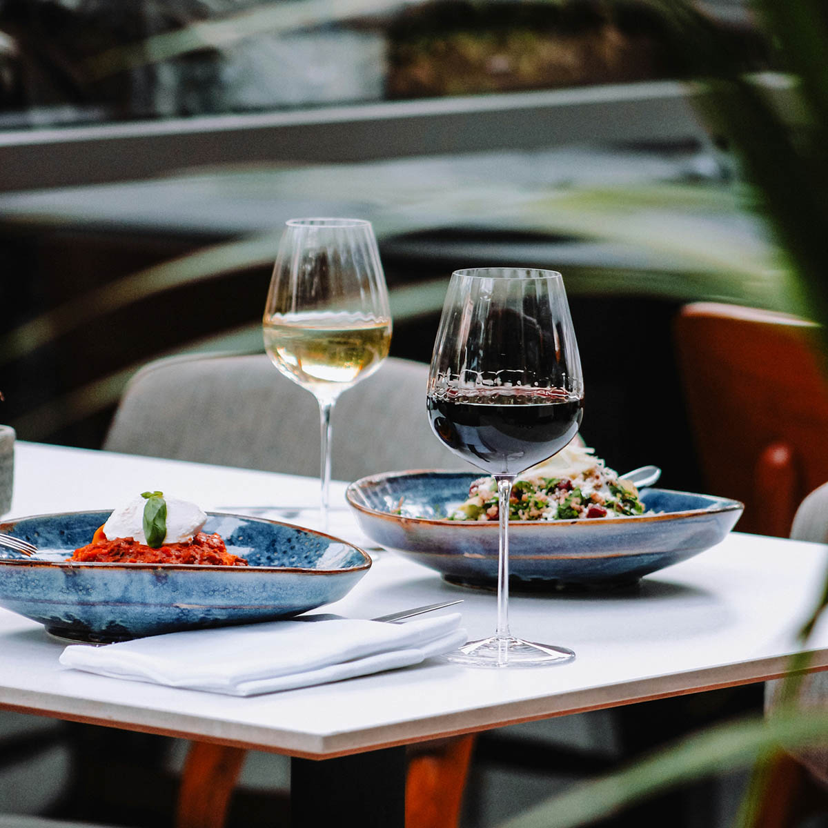 Outdoor dining table with glasses of wine and blue tables with food.