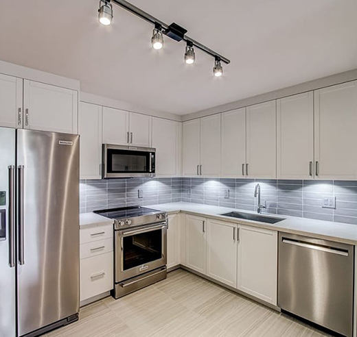 Kitchen with wood style floor, light cabinets, gray tiled backsplash, and stainless steel appliances.