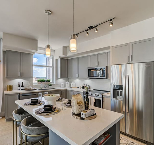 Apartment kitchen with island, stools, gray cabinets, and stainless steel appliances.