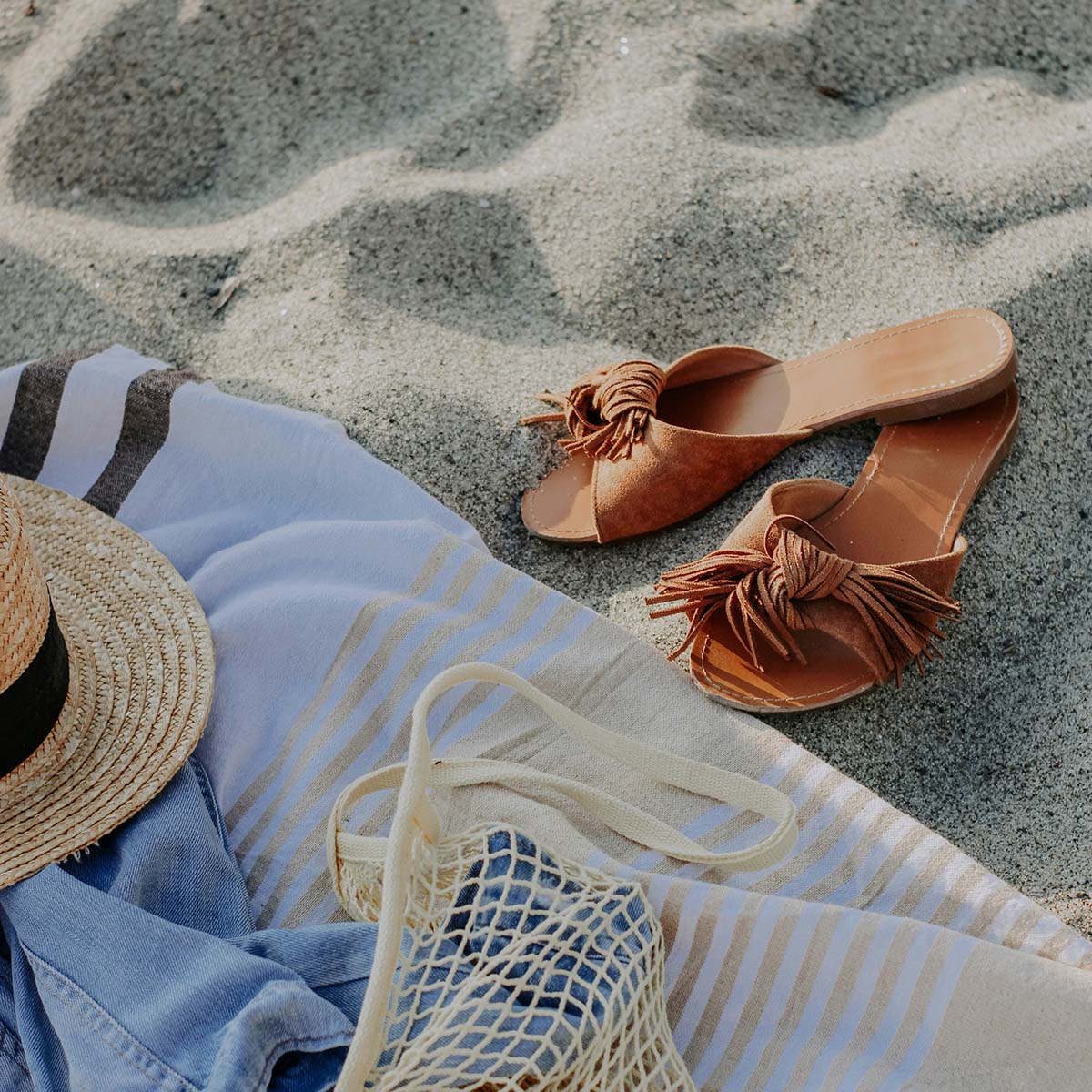 Beach towel in the sand with sun hat, bag, and sandals.