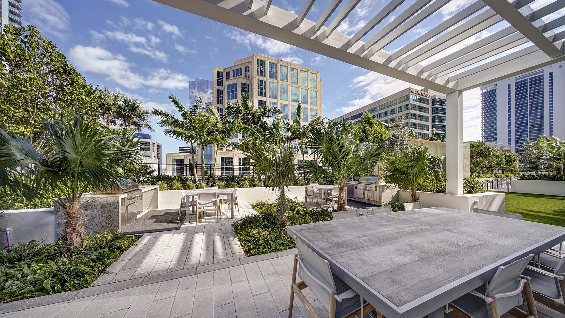 Rooftop lounge with dining table, built in BBQ grills, and lush landscaping.