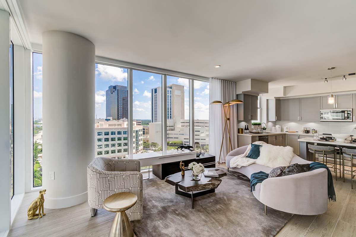 Apartment living area with large windows, plush modern furniture, and contemporary kitchen.